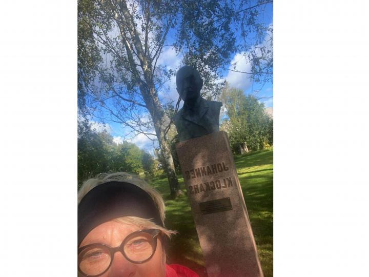 Selfie av en kvinna framför en byst av en man.