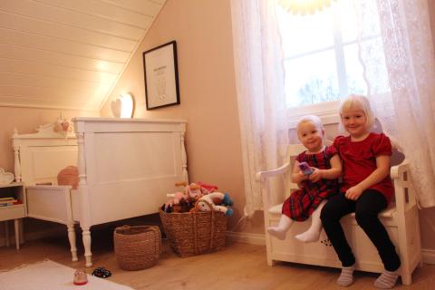 Två små flickor sitter på en säng i sitt rosa barnrum